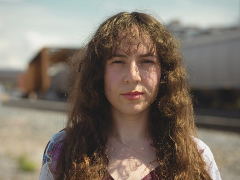 Woman with long brown wavy hair looks at the camera.